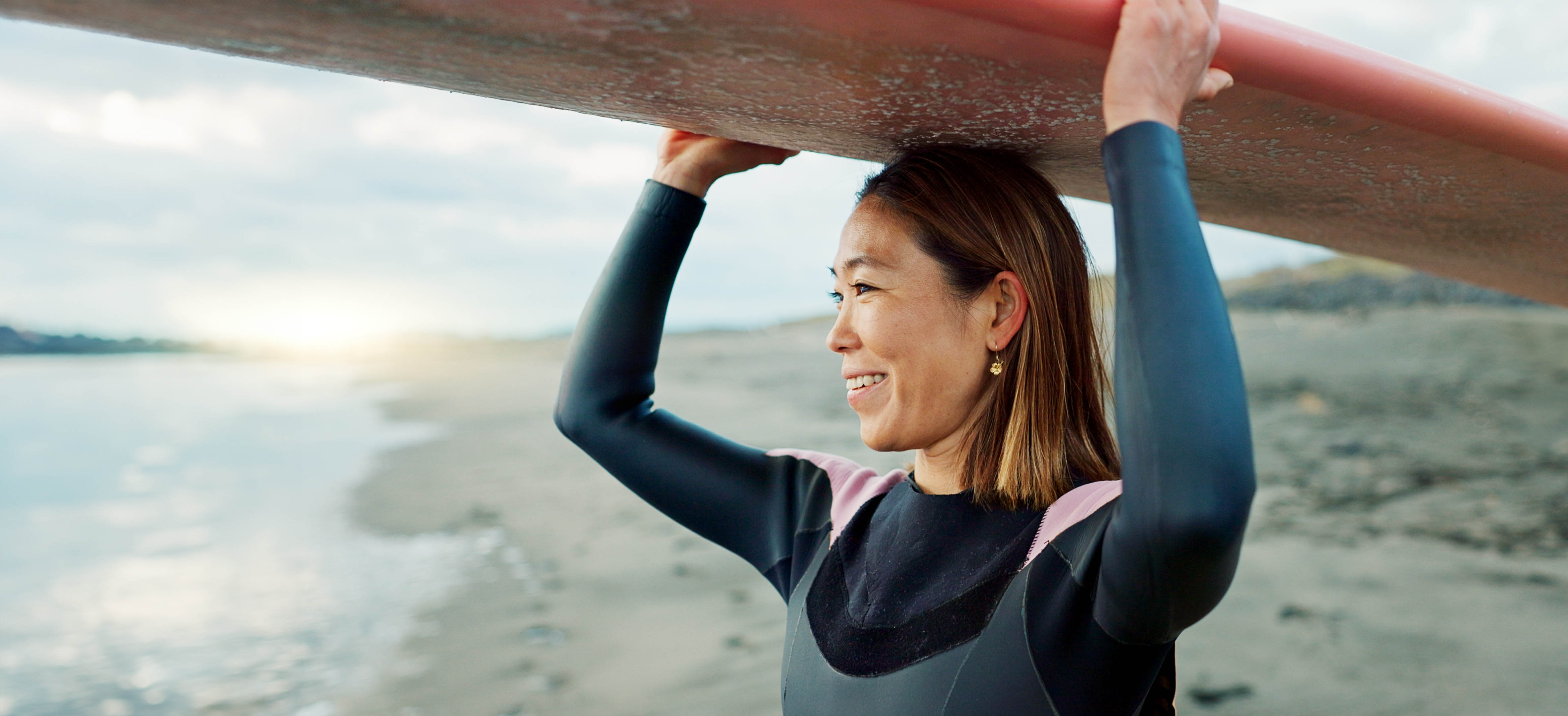 Older woman, smiling looking out to the ocean, with a surfboard on her head